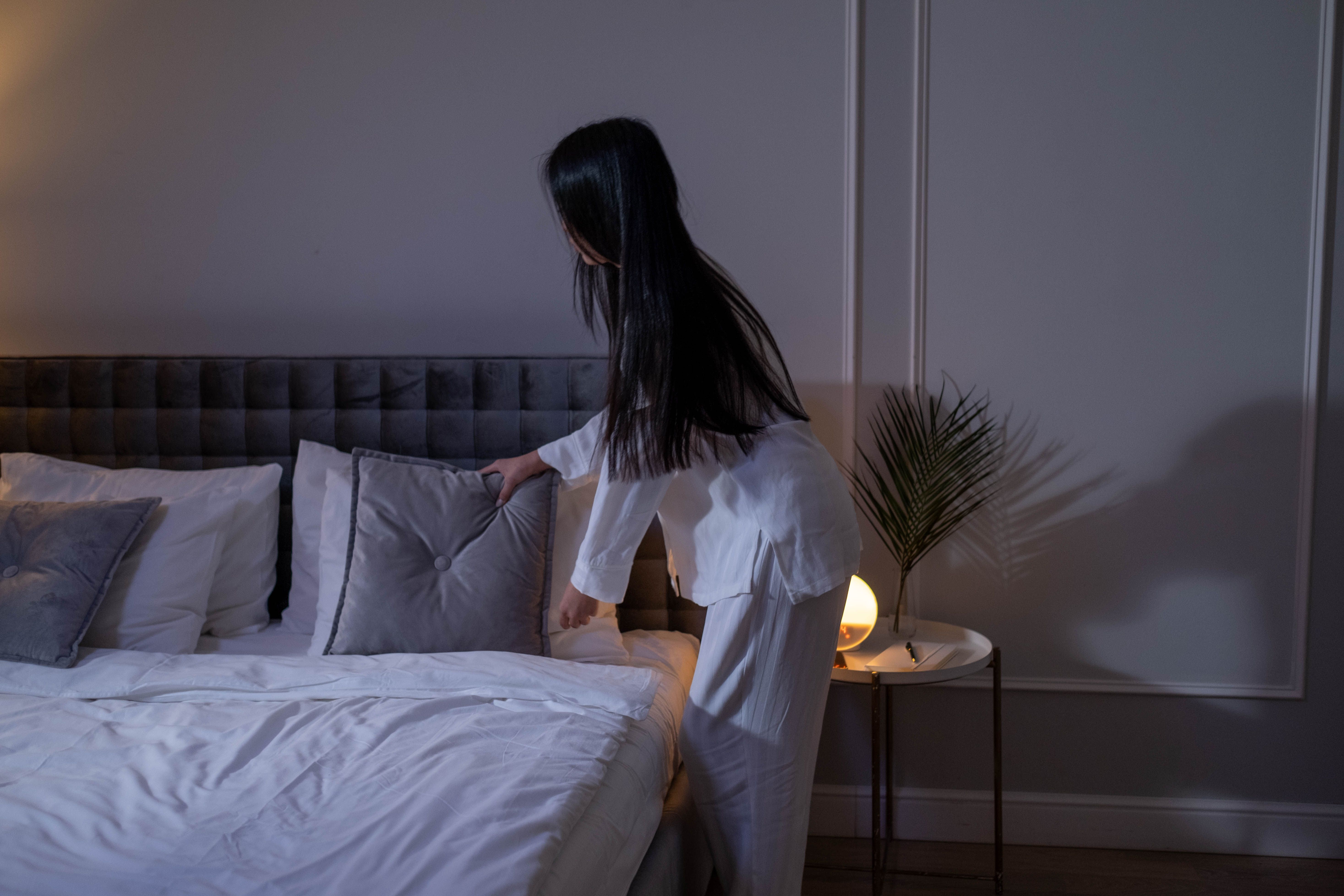A person arranging pillows on a neatly made bed in warm natural light